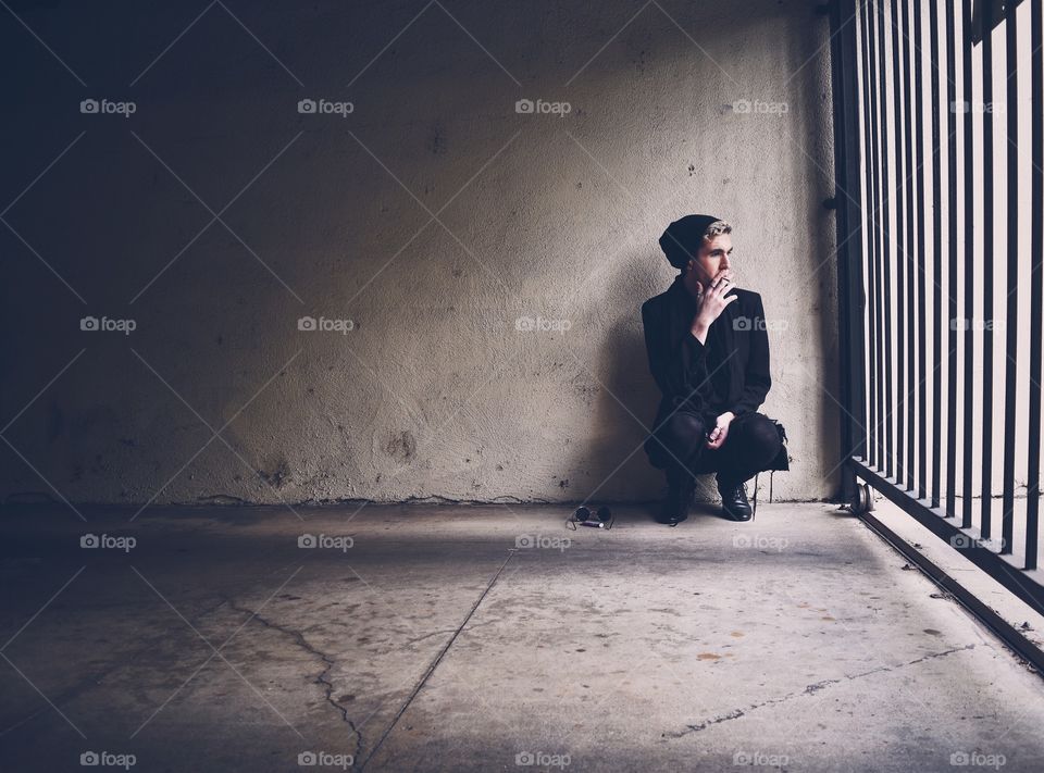 Young man sits against a concrete wall looking outside the parking garage.