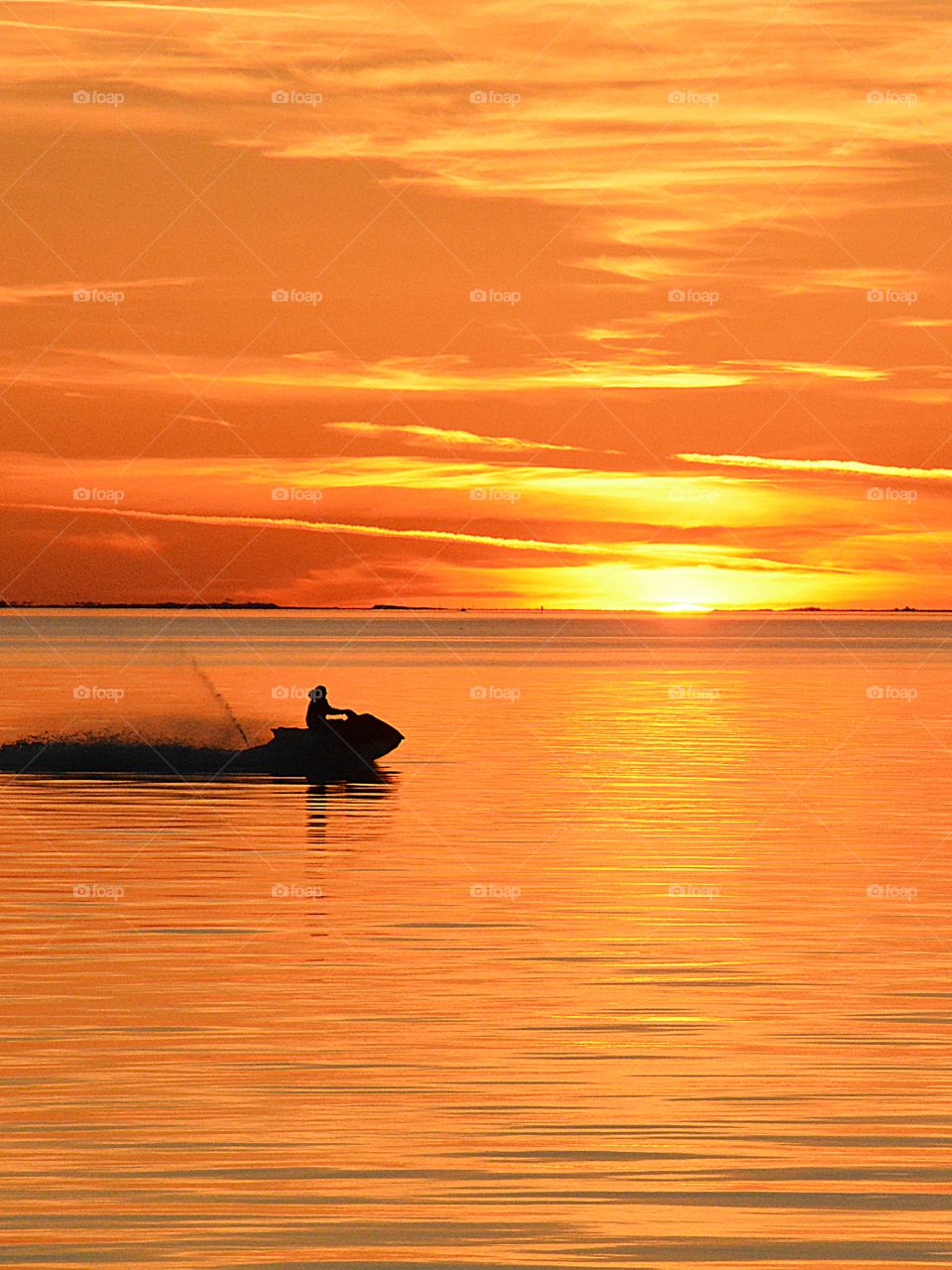 Silhouettes and shadows - A man skims across the shimmering, sun coated bay on his wave runner throwing water behind him as he goes