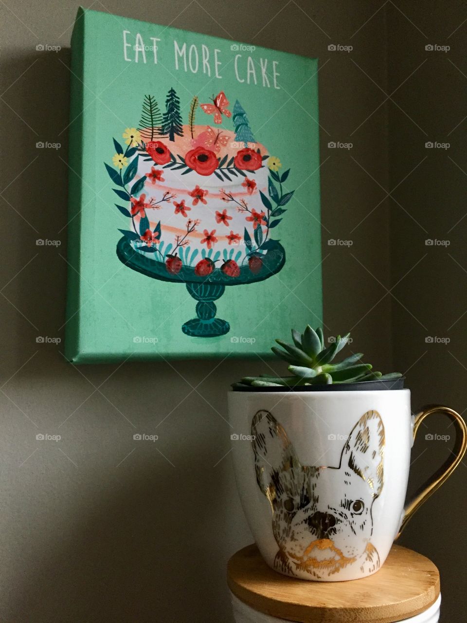 Succulent plant in French bulldog mug with painting “Eat More Cake” behind it