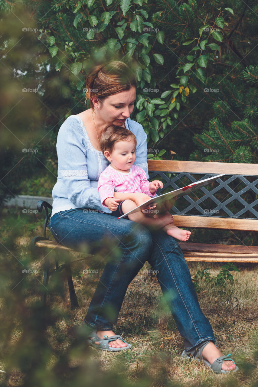 Mother and baby sitting on bench with book