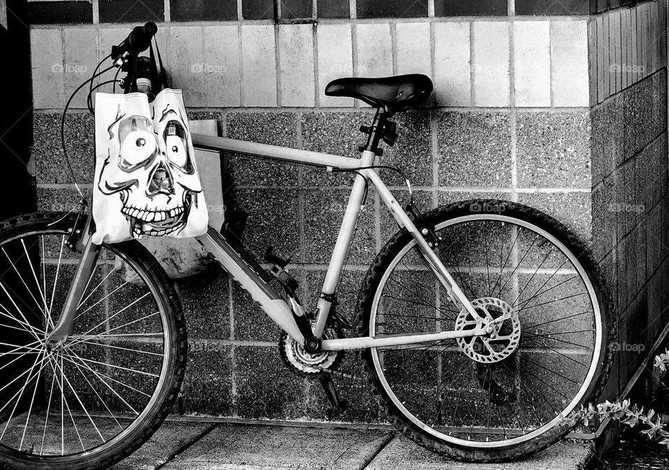 black and white view of a spooky face design shopping bag on a bicycle outside of an Oregon store