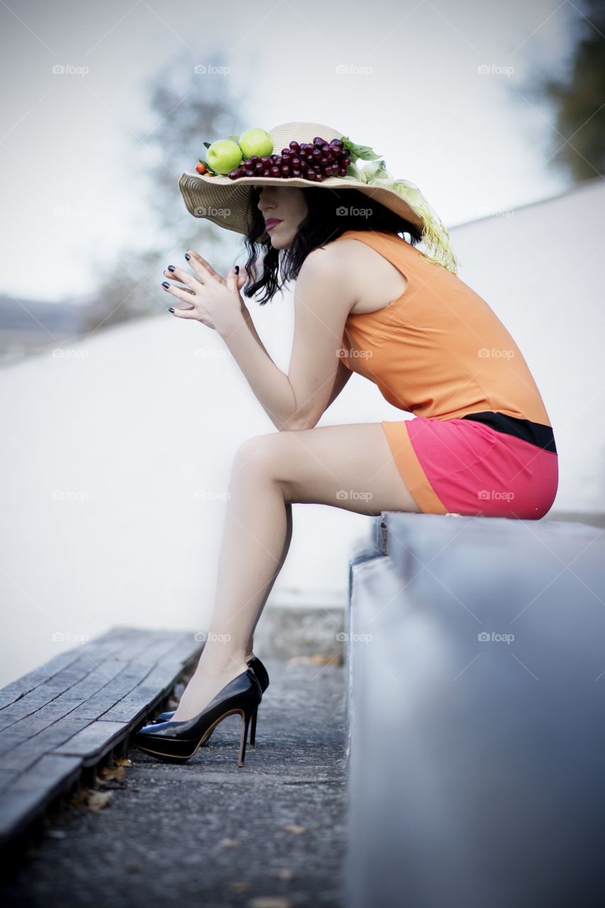 woman in colorful orange dress and big summer hat posing on empty stadium