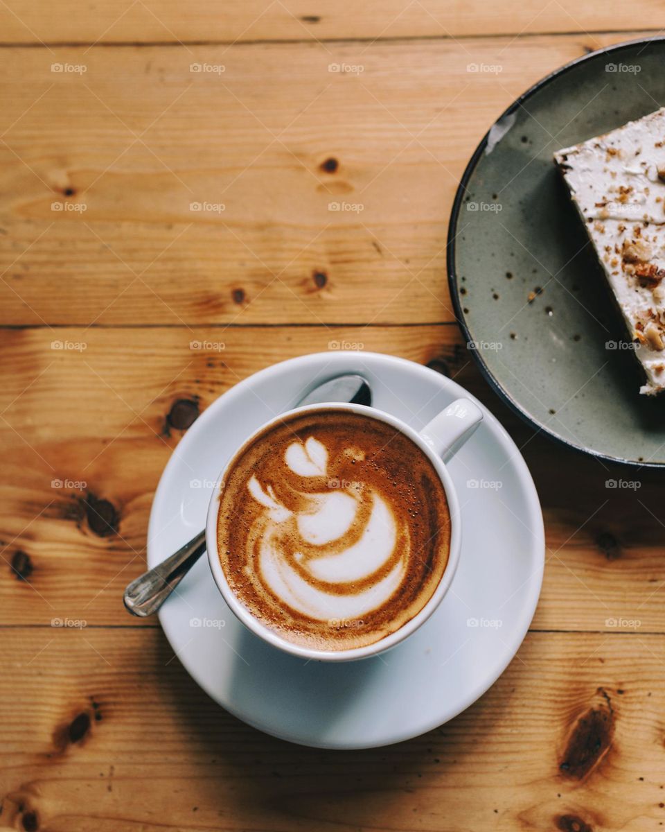 Coffee with latte art and cake on the table in a cosy café 