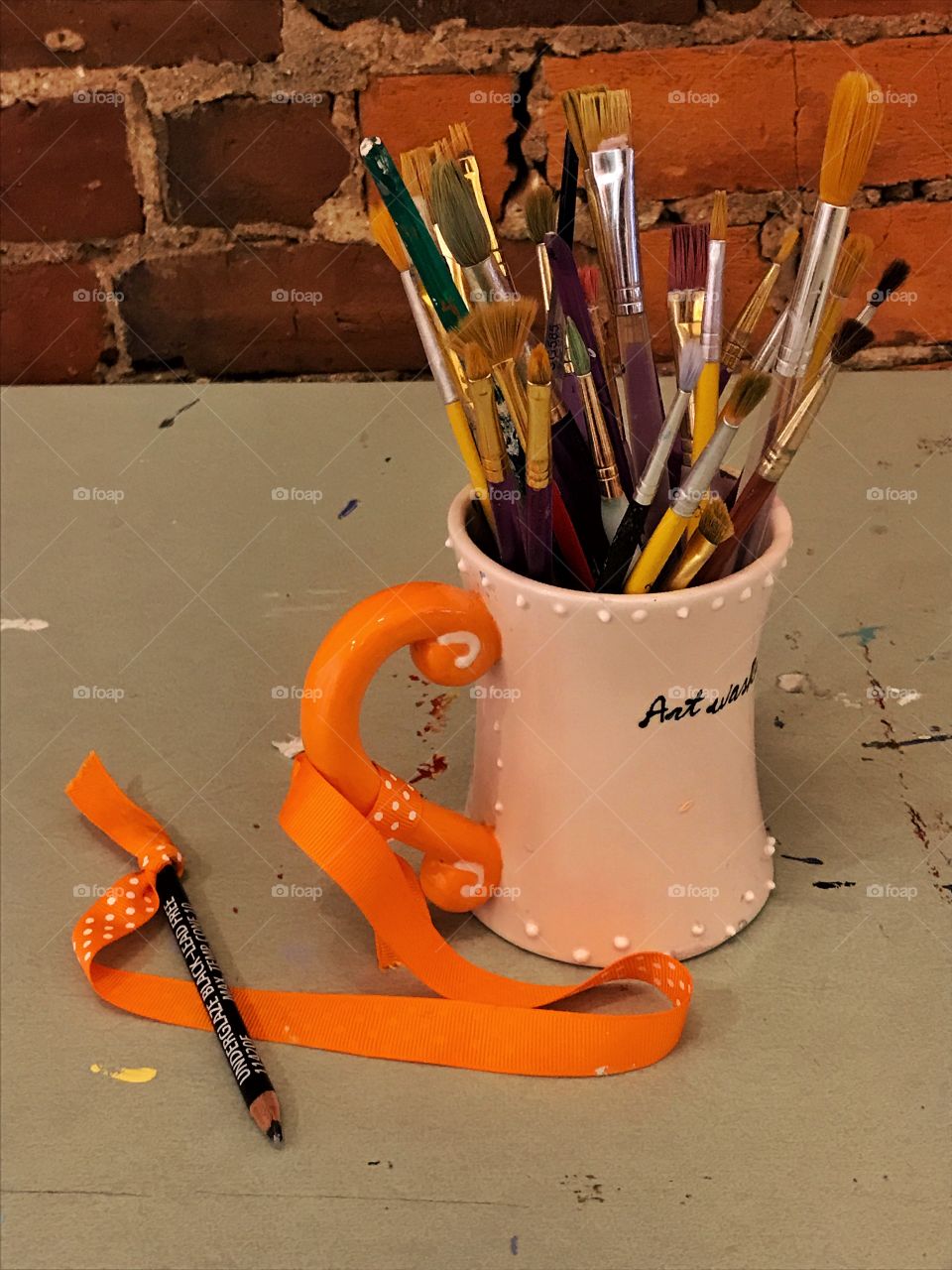 Orange handled mug with orange ribbon and paint brushes with orangish wall background 