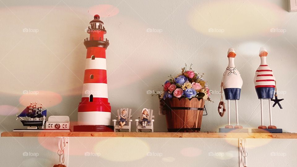 lighthouse theme on the shelf. decorated interior wall shelf  with items like mini lighthouse, vintage flower bucket, sailor dolls, boat and treasure