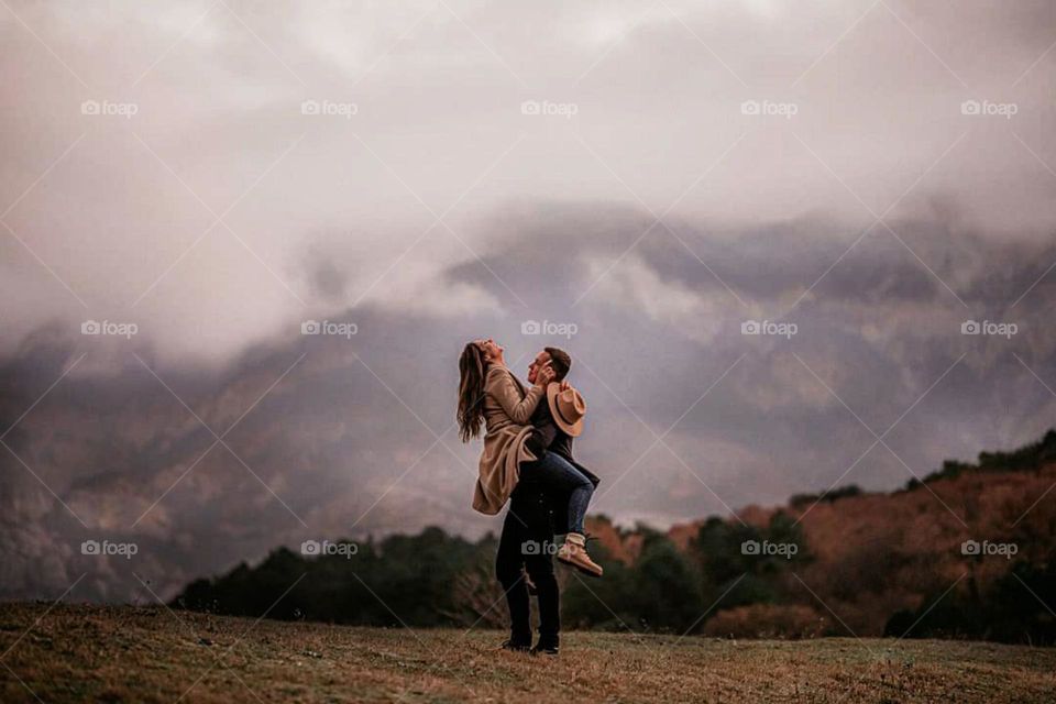 Portrait of two people standing in nature against a backdrop of mountains and cloudy skies