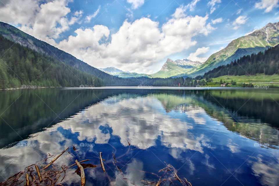 Alpine lake of blue water where the clouds, the mountains and the forests of green pines that surround it are reflected.