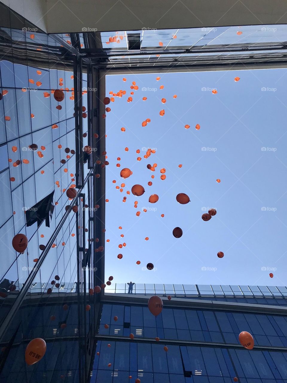 Helium balloons in the air close to a glass building and a man watching