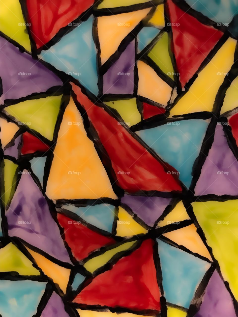 Clash of colours: A closeup of a ceramic plate painted & fired by my daughter. Vibrant triangular geometric shapes in shades of orange, red, green, purple & turquoise bordered in black. Seemingly mismatched colours but it works!