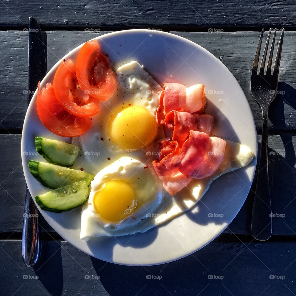 Breakfast overhead shot, eggs with beacon, tomatoes and cucumber on wood desk