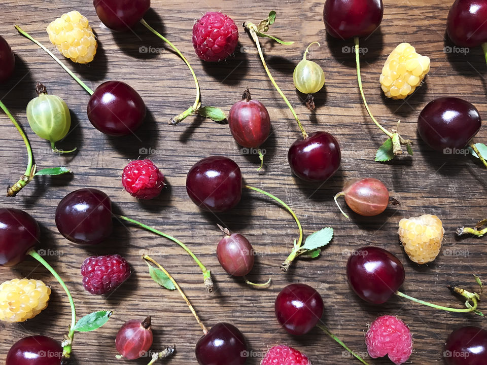 Colorful berries - red cherries, red and white raspberries, green gooseberries on rustic wooden background 