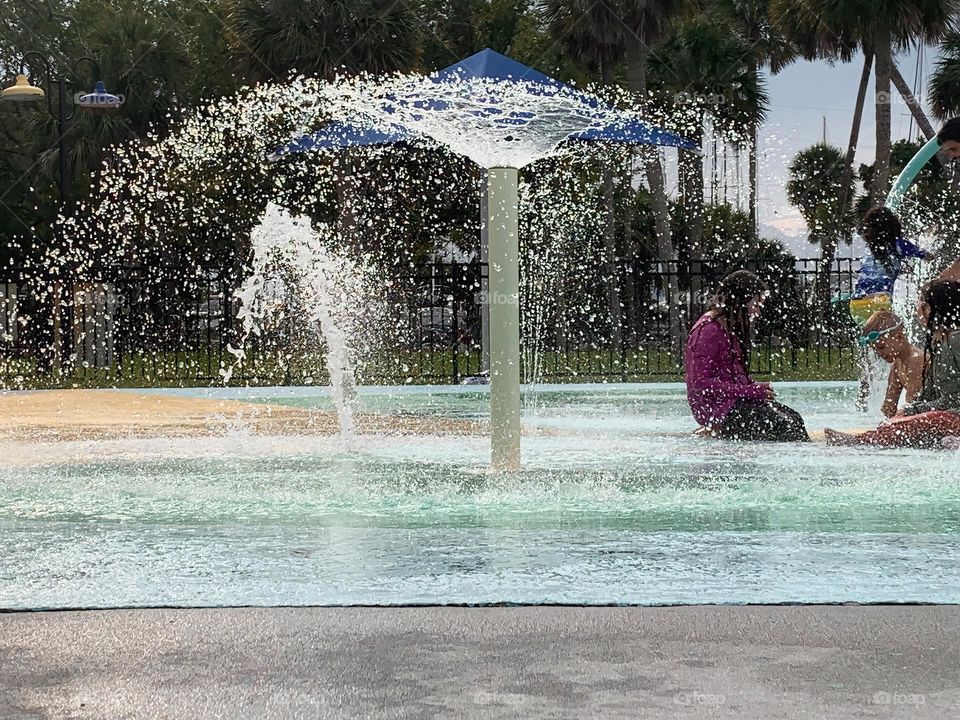 Children having lots of fun in the water at the colorful kids splash pad at the city park for children during a really warm day in Florida.