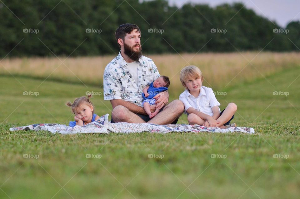 A dad sitting at the park with his 3 grumpy children. Such a funny photo