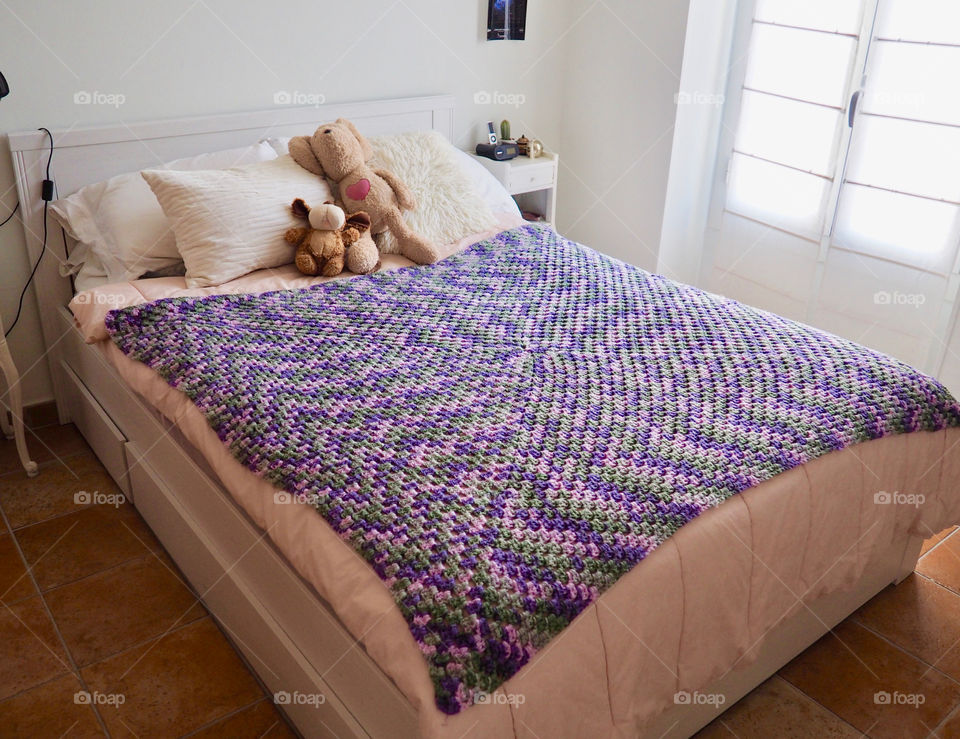 Shades of purple hand made crochet blanket on girl’s bed.