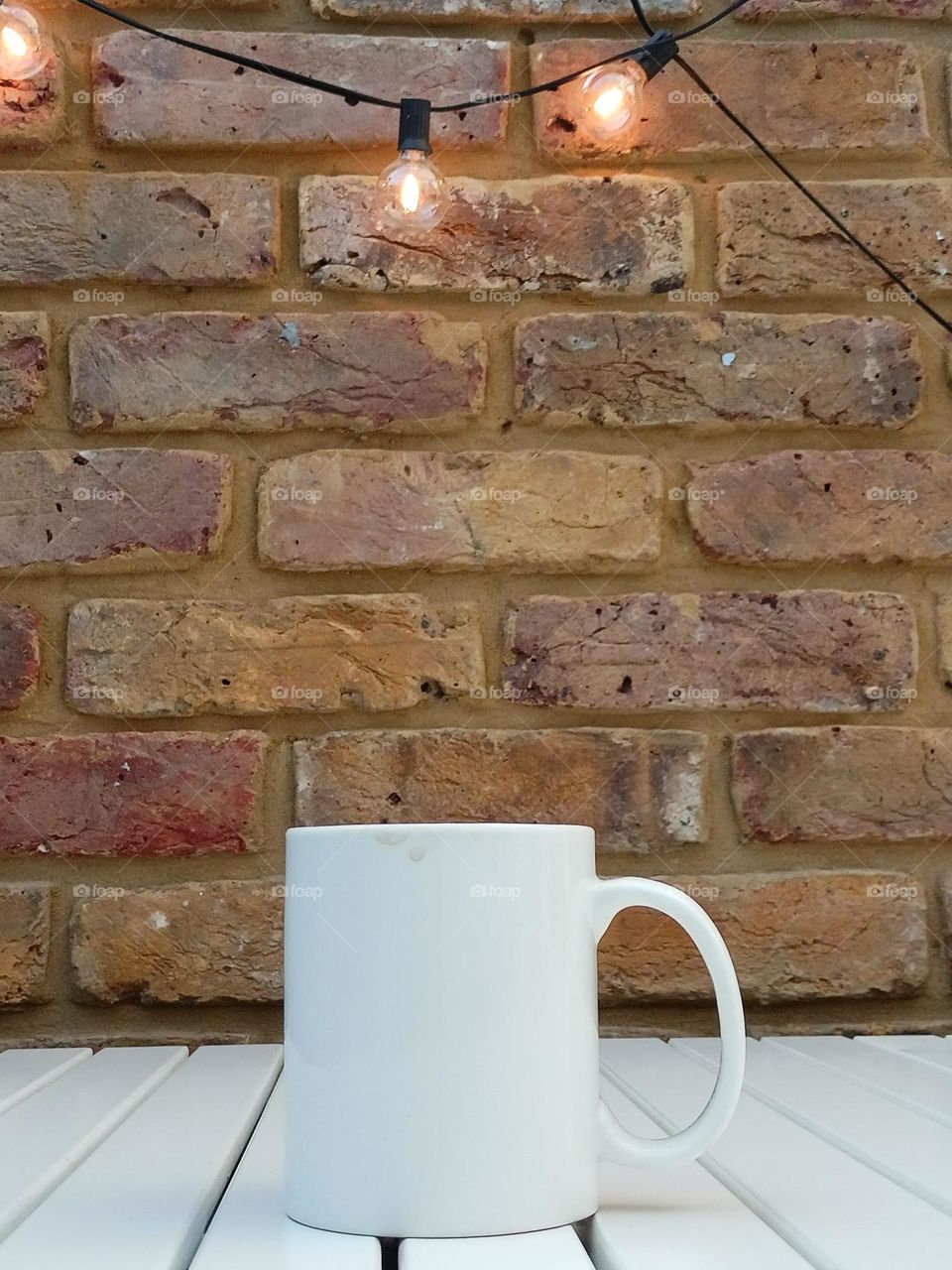 White cup against brick wall with light bulbs