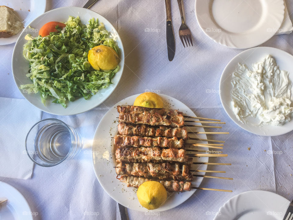 Plates in a table with greek meal pork souvlaki, tzatziki and green salad in a greek taverna. Flat lay shot.