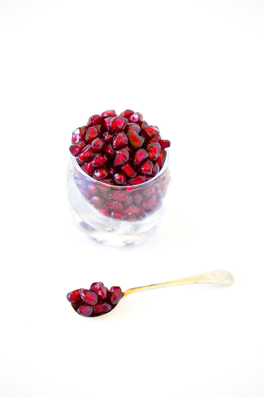 Glass with fresh pomegranate seeds with single golden spoon, minimalist image on a white background. Love this red juicy fruit for summer. Close up.