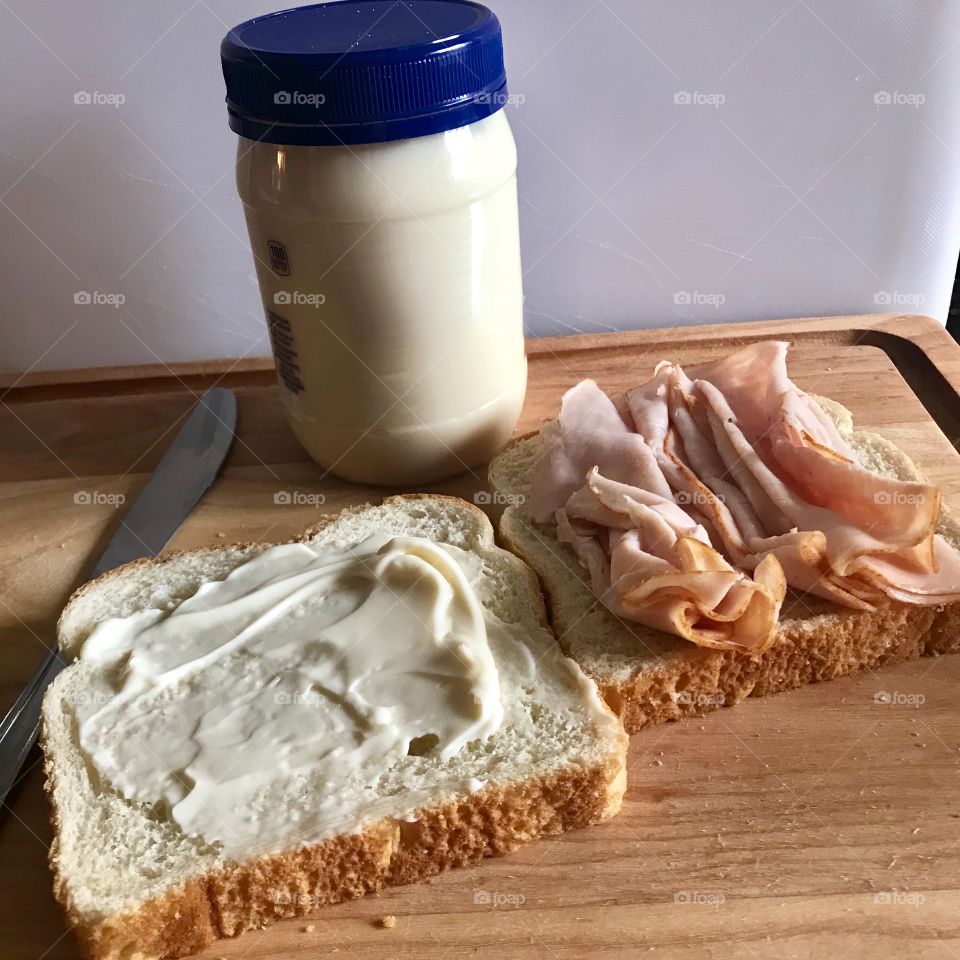 A yummy Turkey sandwich with mayonnaise on a wooden cutting board in the kitchen for lunch. 