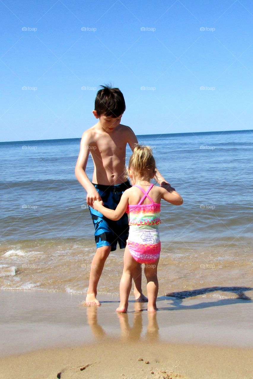 Family beach time . Brother telling his sister to not be afraid of the water 