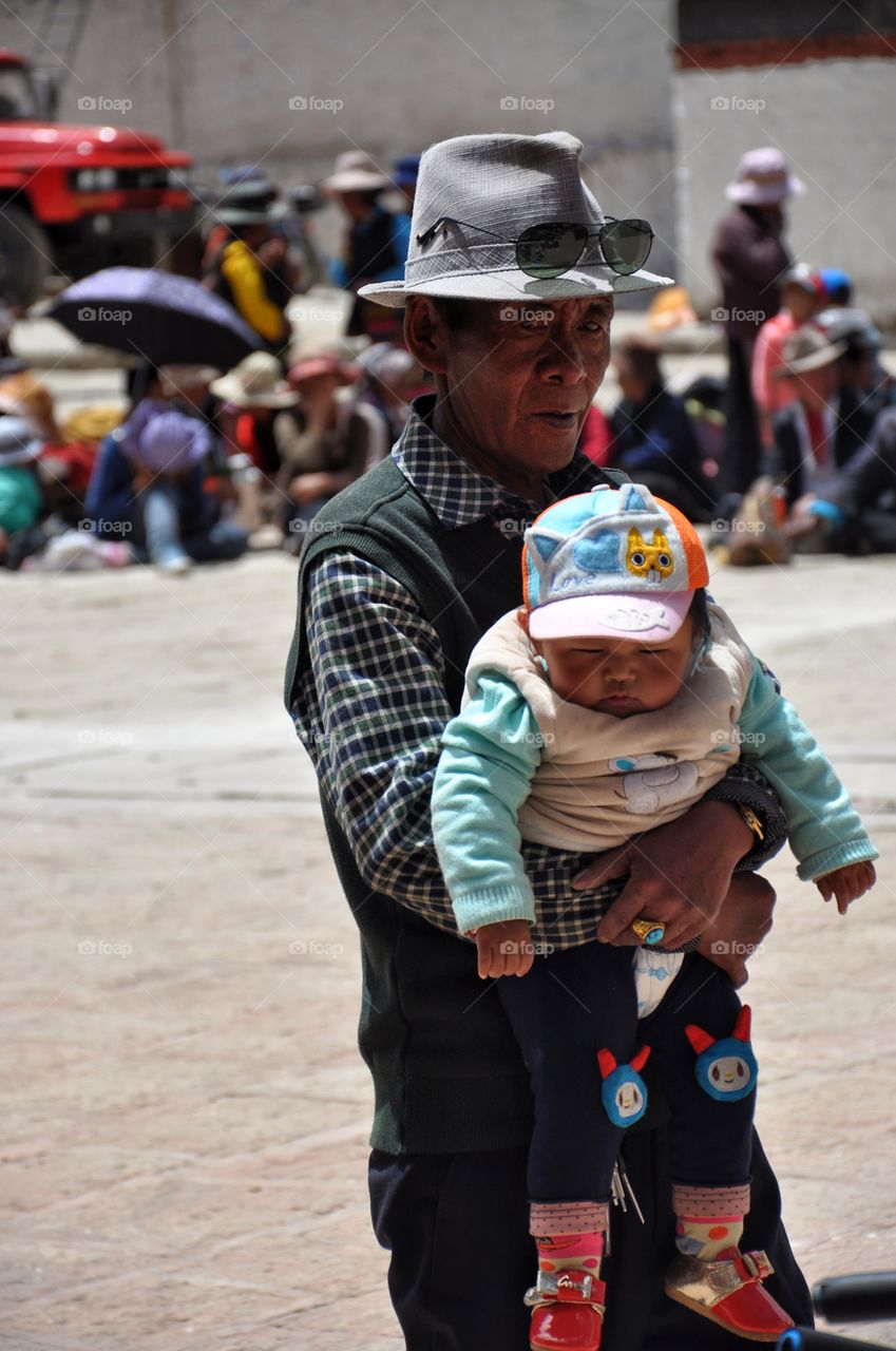 old tibetan man holding little cute baby in the yard of buddhist monastery in shigatse