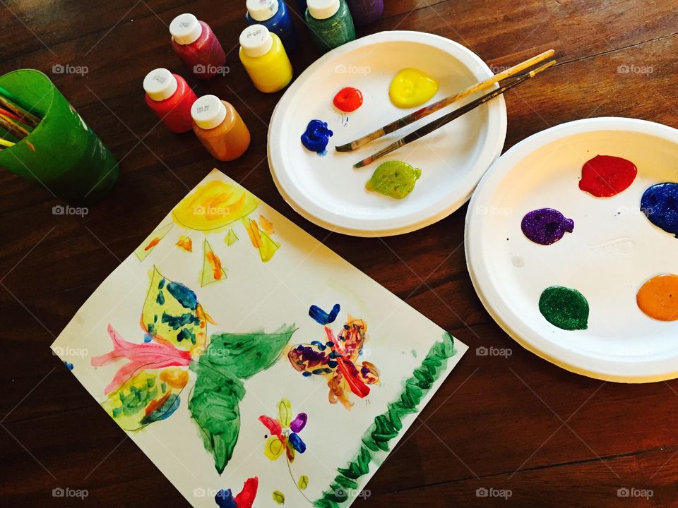 Colorful child's painting of butterflies with paints and brushes