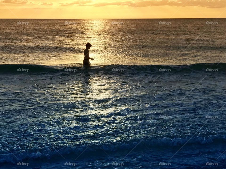 Small boy in the ocean immersed in golden sunlight .