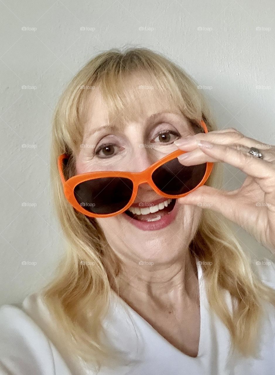 Woman laughing putting on orange sunglasses 