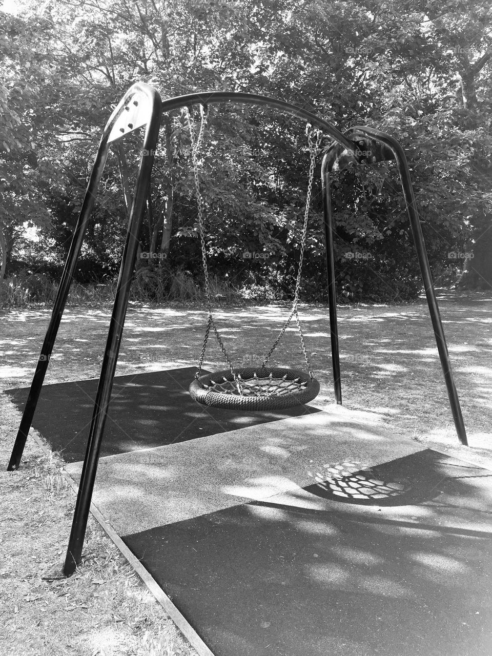 A shady, shadowy picture of a small, peaceful park taken in the early morning. A welcoming swing awaits the first child. 