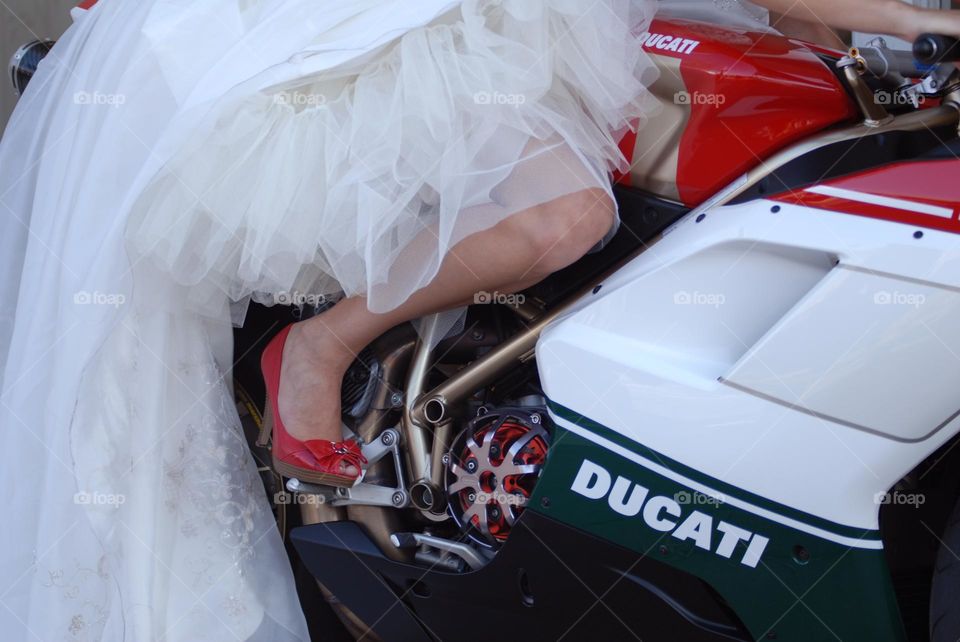 A detailed view of a bride sitting on a motorcycle wearing red shoes and a white wedding dress