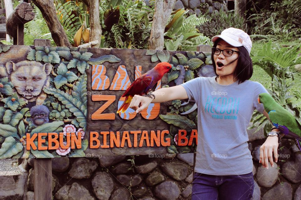 Bali, Indonesia - 1 May 2023 : Portrait of a female tourist in a hat with a cockatoo in both hands taking a photo at the Bali Zoo, with a happy expression