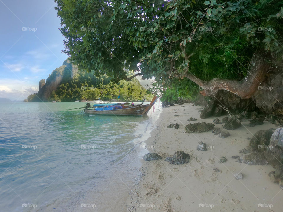 Precioso paisaje de playa Tailandesa con vegetación y montañas de fondo acompañado con bote en el mar