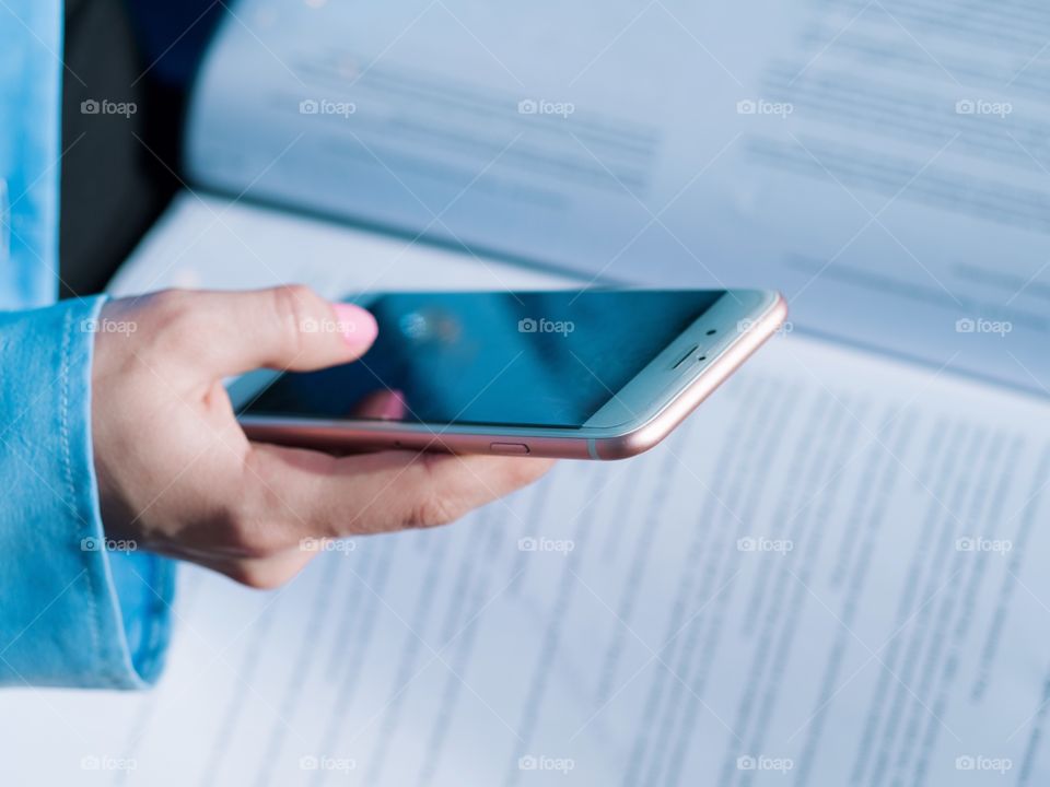 Female hands using smartphone with documents 