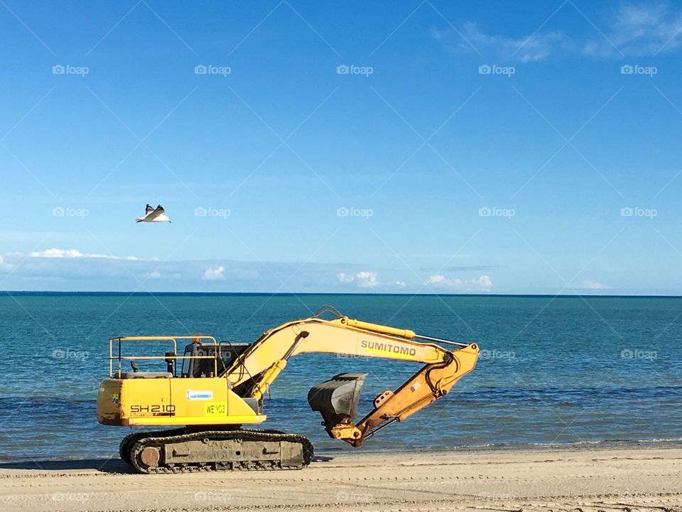 Sumitomo yellow excavator heavy machinery traveling along south Australian beach for sand maintenance 