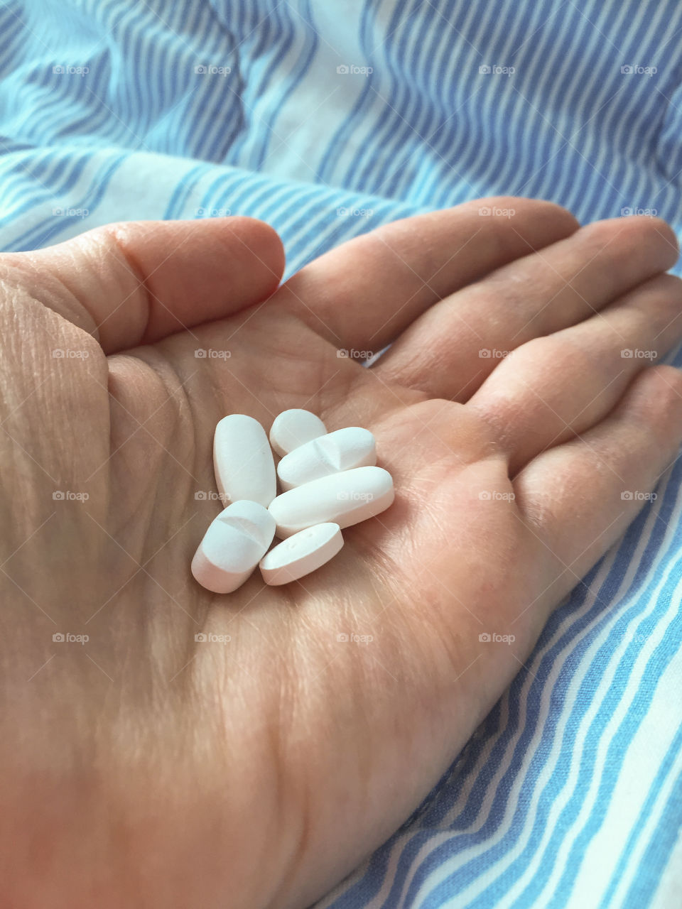 Hand holding a dose of medicine and with a hospital bed in the background.