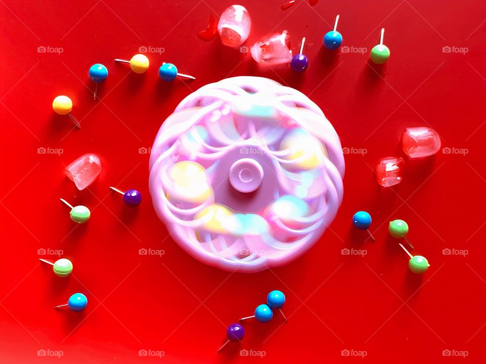 Multicolor Fidget Spinner Time In Motion Long Exposure Seems To create Cold Ice Cubes On A Red Background.