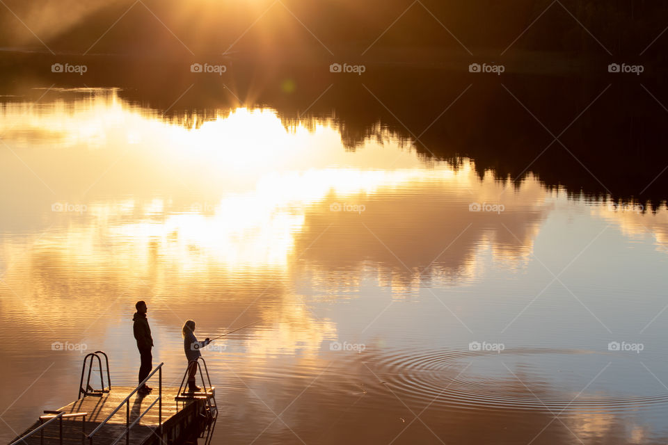 Fishing at colorful sunset, beautiful reflection on mirror lake 