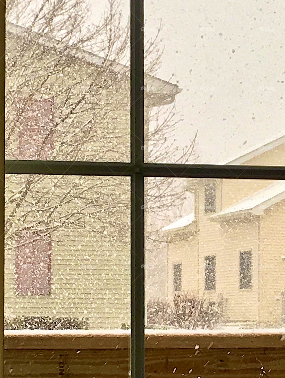Pouring snow in urban area through glass pane window facing apartment units in winter