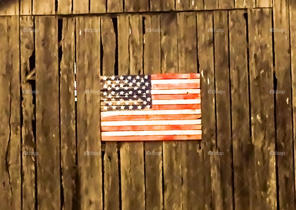 The American flag proudly displayed,for all to see, on the side of an old rustic barn. 