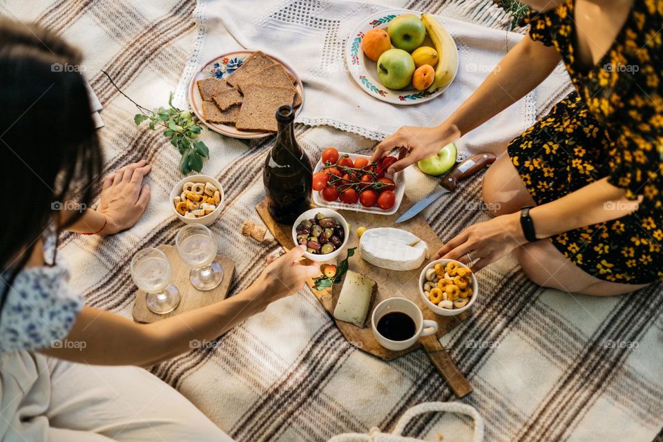 Two women enjoying a lovely picnic in the garden, with fresh fruits, vegetables, cheese and bread, in summer time.