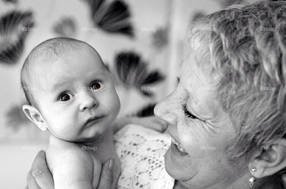 A WHITE GRANDMOTHER SMILES BROADLY AT HER NEWBORN WHITE GRANDSON, WHO