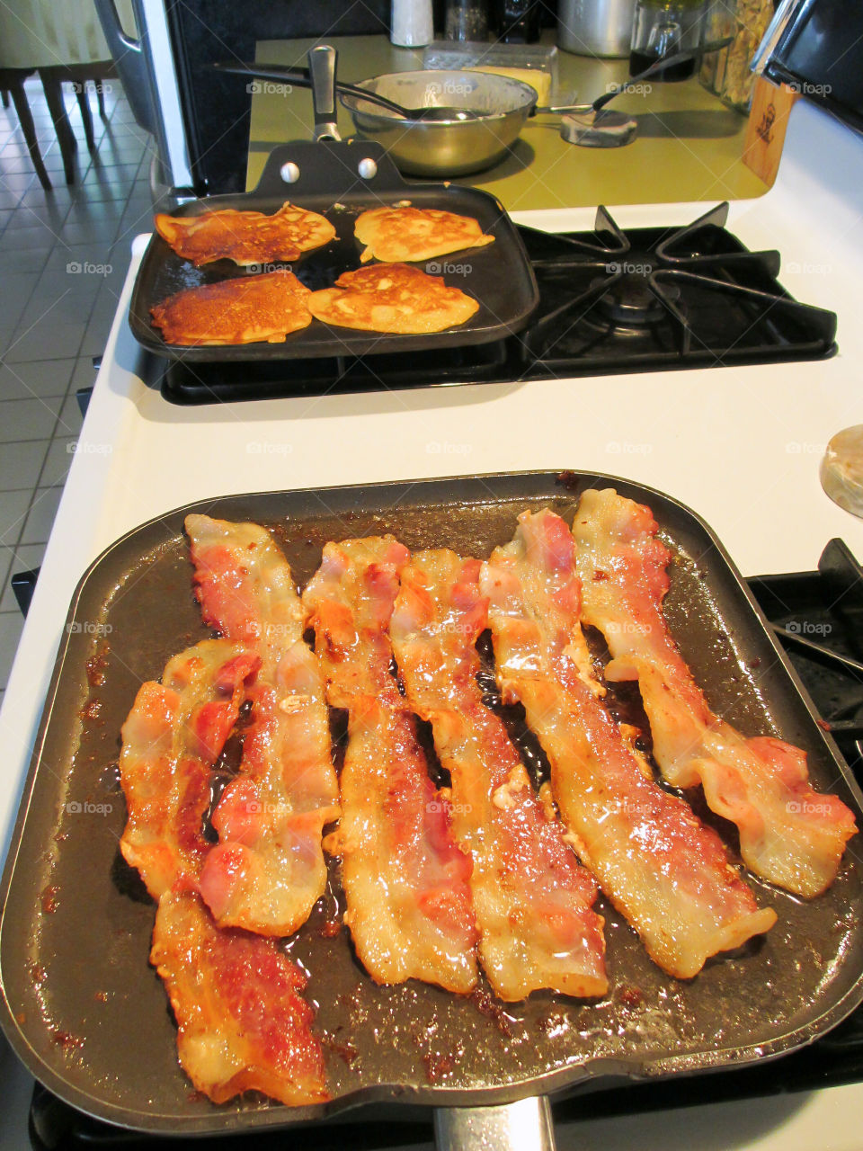 Breakfast is Cooking. Bacon and pancakes cooking on a stove top