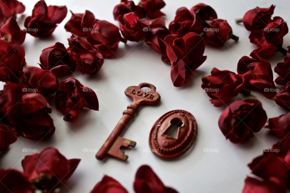 Red, metal, vintage key and keyhole with red, silk rose buds on white marble surface