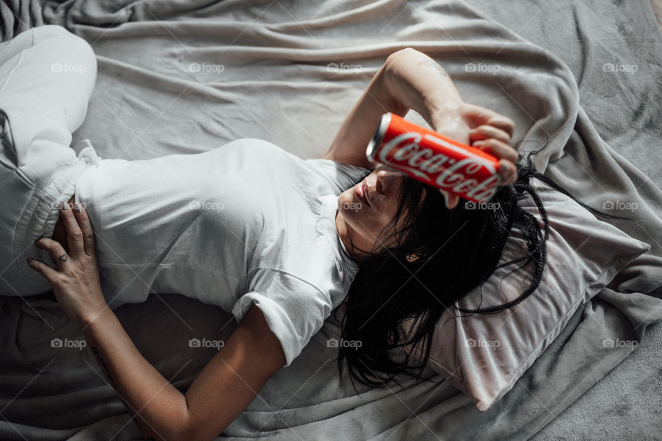 the girl lies on the bed and holds a Coca Cola