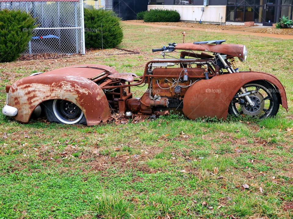 A rusty motorcycle cobbled together from multiple vehicles sits on grass