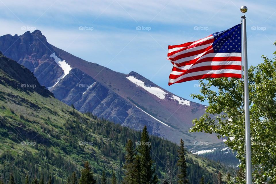 An American flag flies in the foreground of large mountains at Glacier National Park in Montana