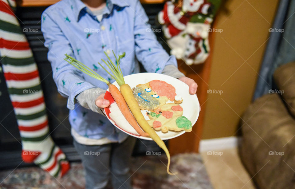Young boy holding a small plate of cookies and carrots to leave out for Santa and reindeer