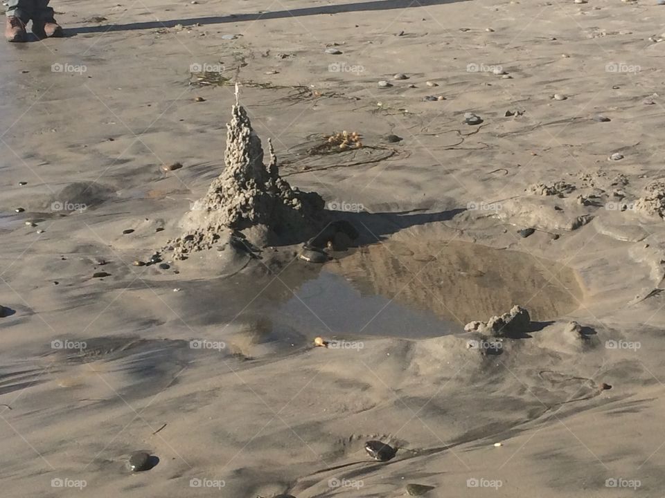 A pointy sandcastle in front of its own small lake on the beach. 