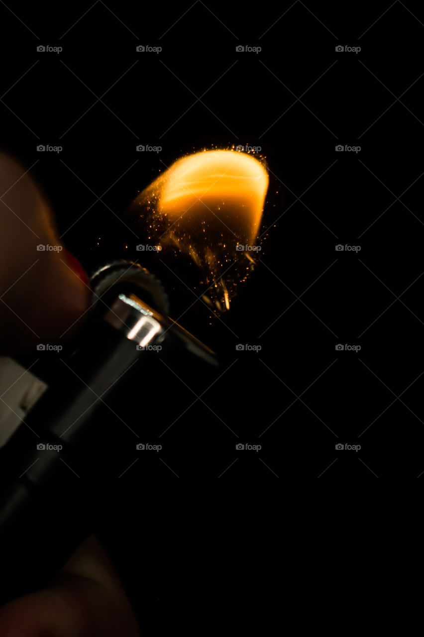 A person has lighters in his hands and he lights it through a flint wheel, the lighter ignites, sparks and fire appear, close-up on a black background.