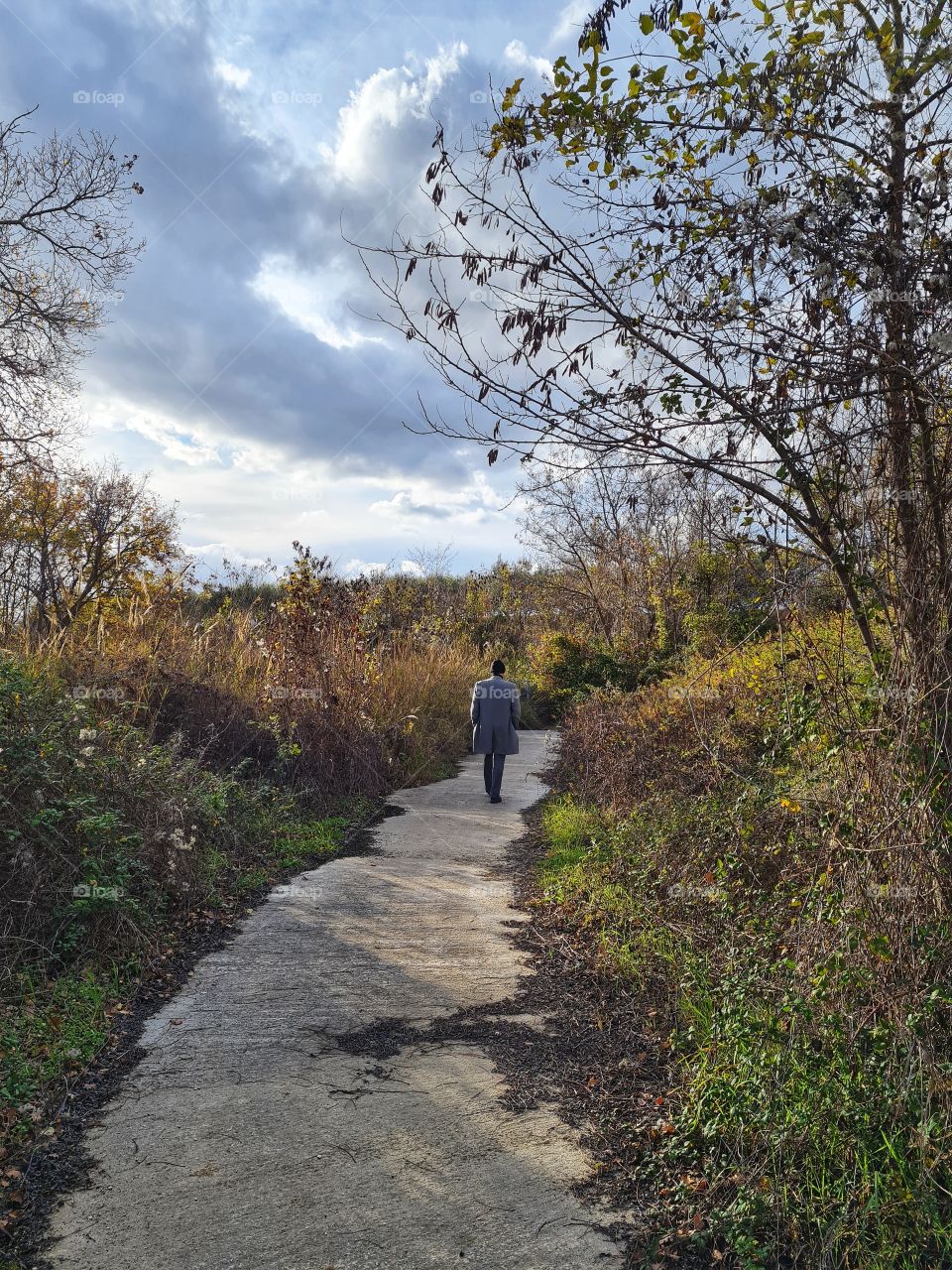 man from behind with coat walks alone a country path