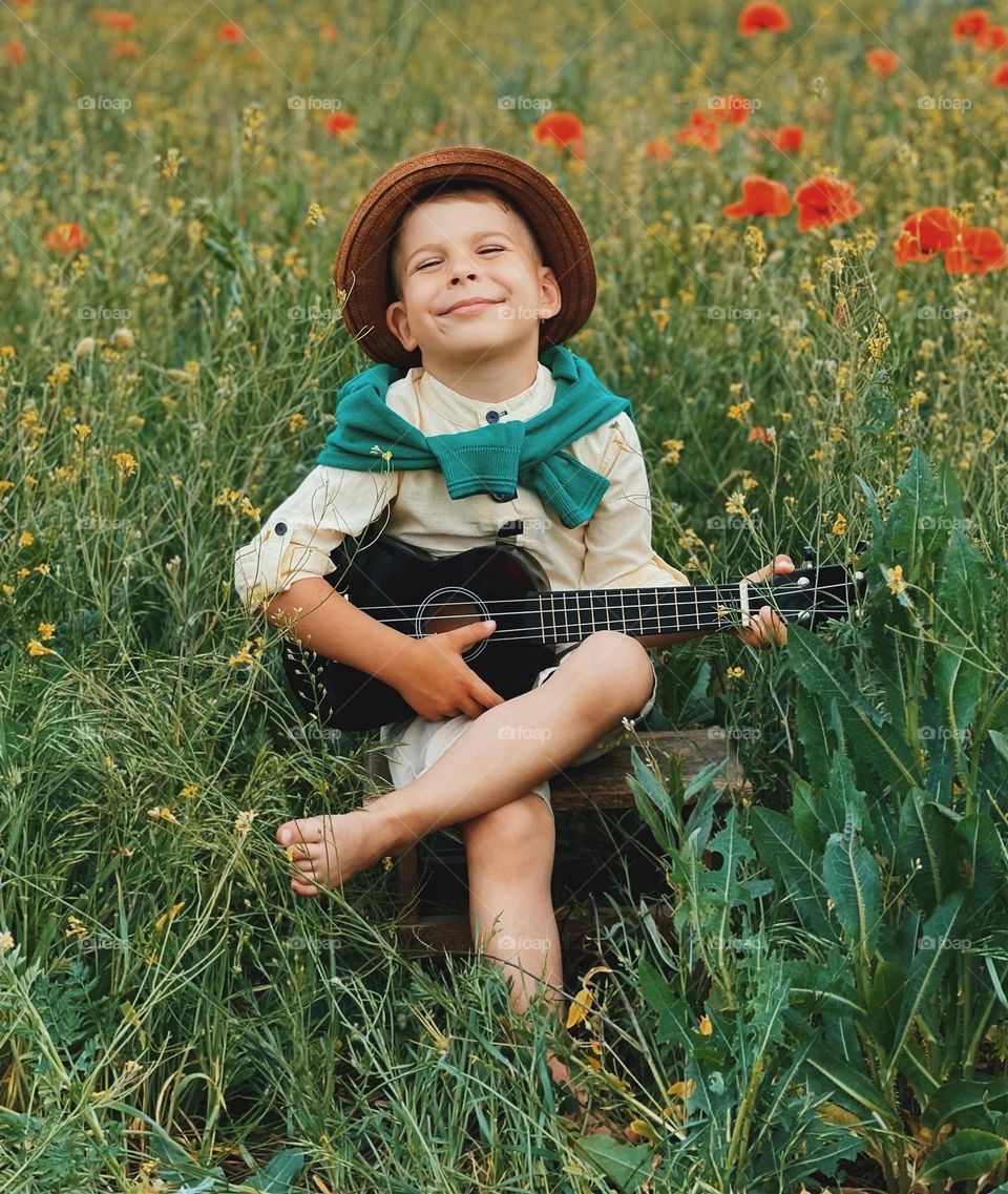 A cute little BOY toddler playing on the guitar between flowers